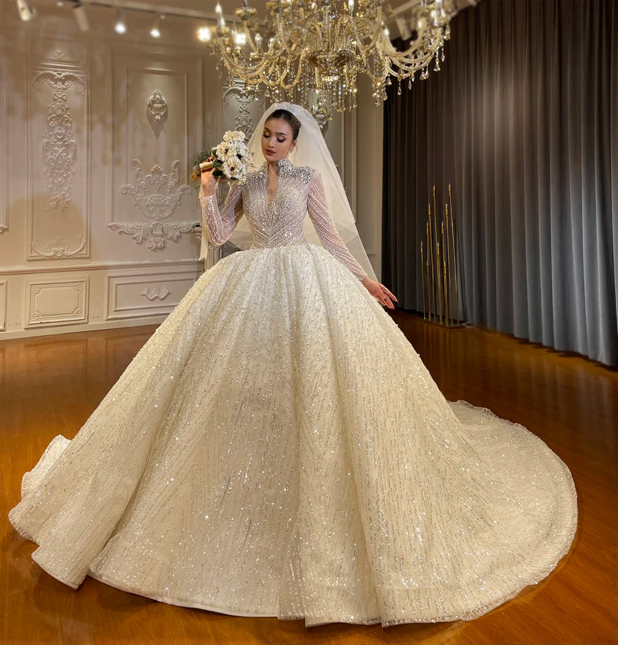 Full front view of a shimmering long sleeve wedding dress with a voluminous ball gown skirt and intricate silver embroidery in a luxury bridal showroom.