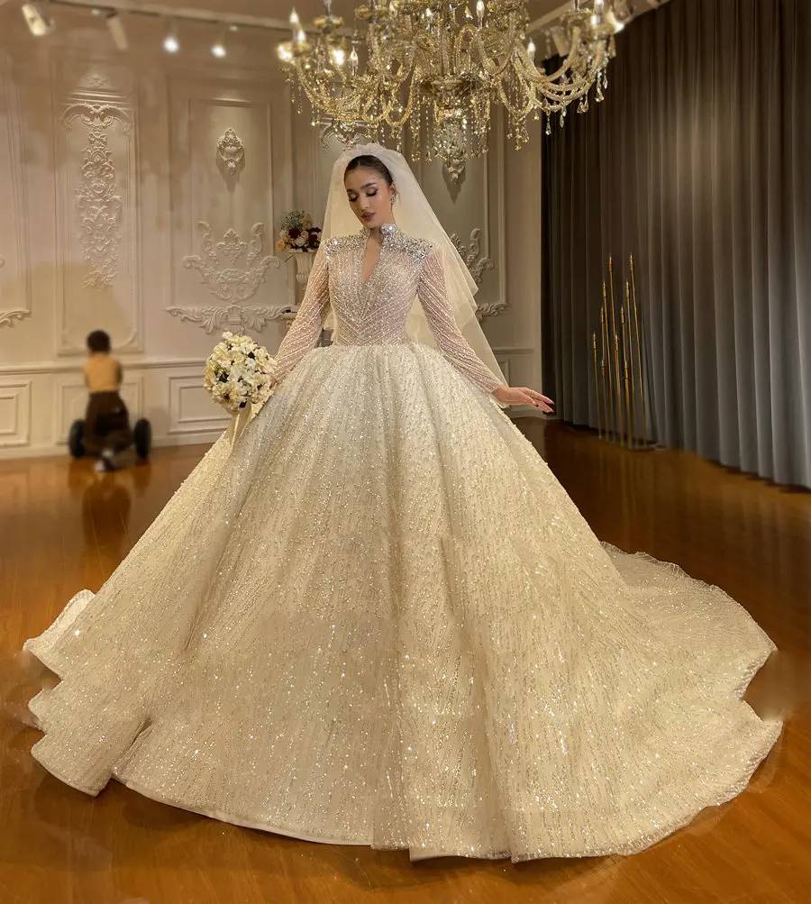Front-side angle of a beaded luxury wedding gown on a mannequin, emphasizing the sheer shimmering long sleeves and the reflective crystal-patterned bodice.