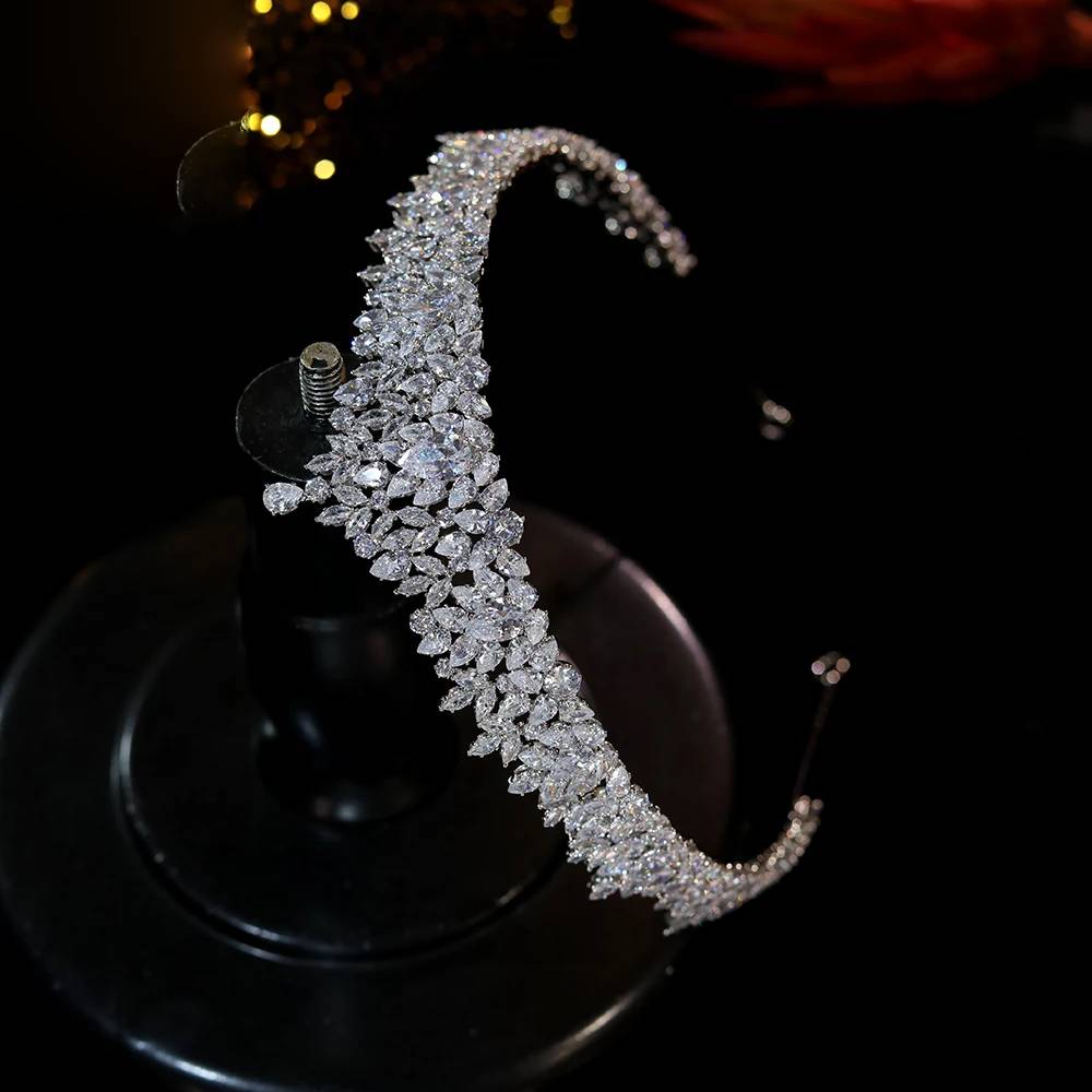 Side-profile view of a silver-plated queen crown bridal headpiece, showcasing the dense pave cluster details on a black stand.
