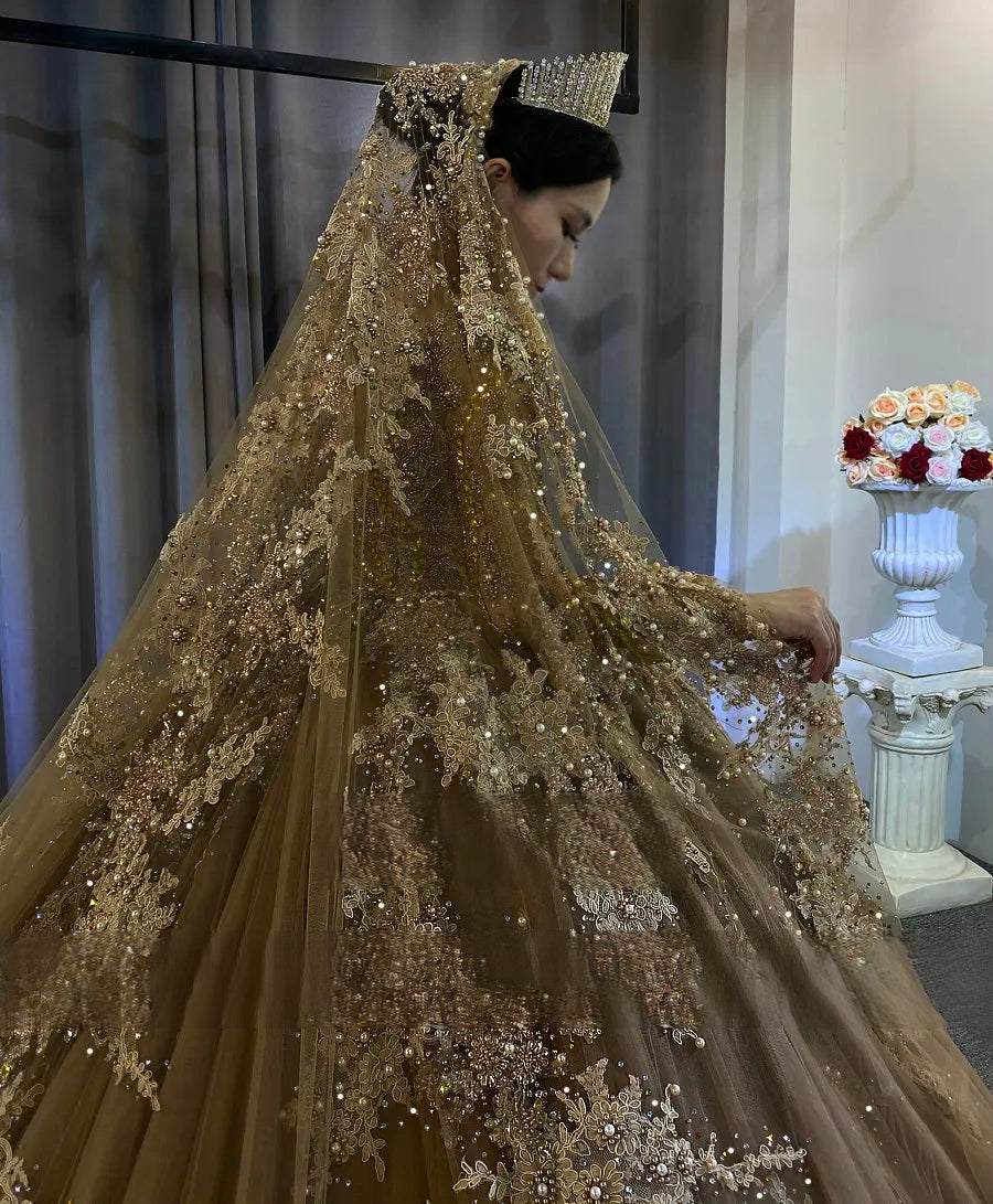 Detailed side view of a luxury champagne wedding veil with heavy lace embroidery and the shimmering beaded long sleeves of the bridal gown.