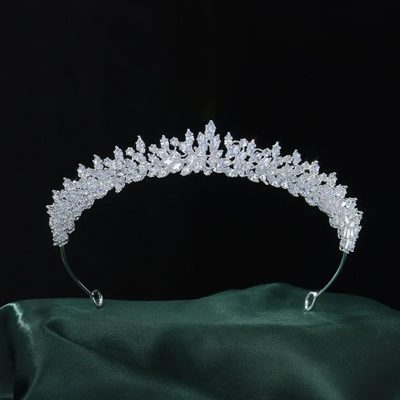 A silver crystal bridal crown resting on a green fabric base, ready for a special occasion.