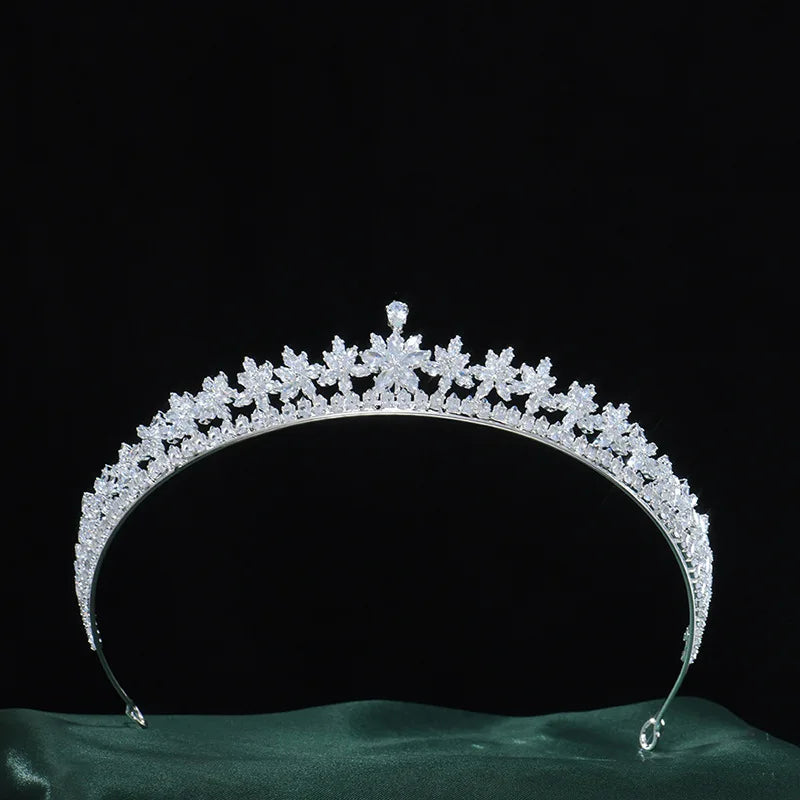 A detailed view of a sparkling crystal bridal tiara crown resting on a green fabric base against a black backdrop.