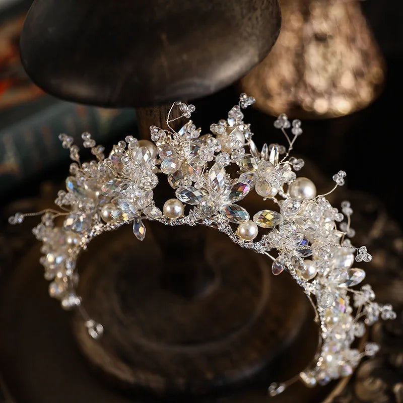 A delicate princess crown wedding tiara crafted with crystals, freshwater pearls, and fine silver wiring, displayed on a wooden stand.