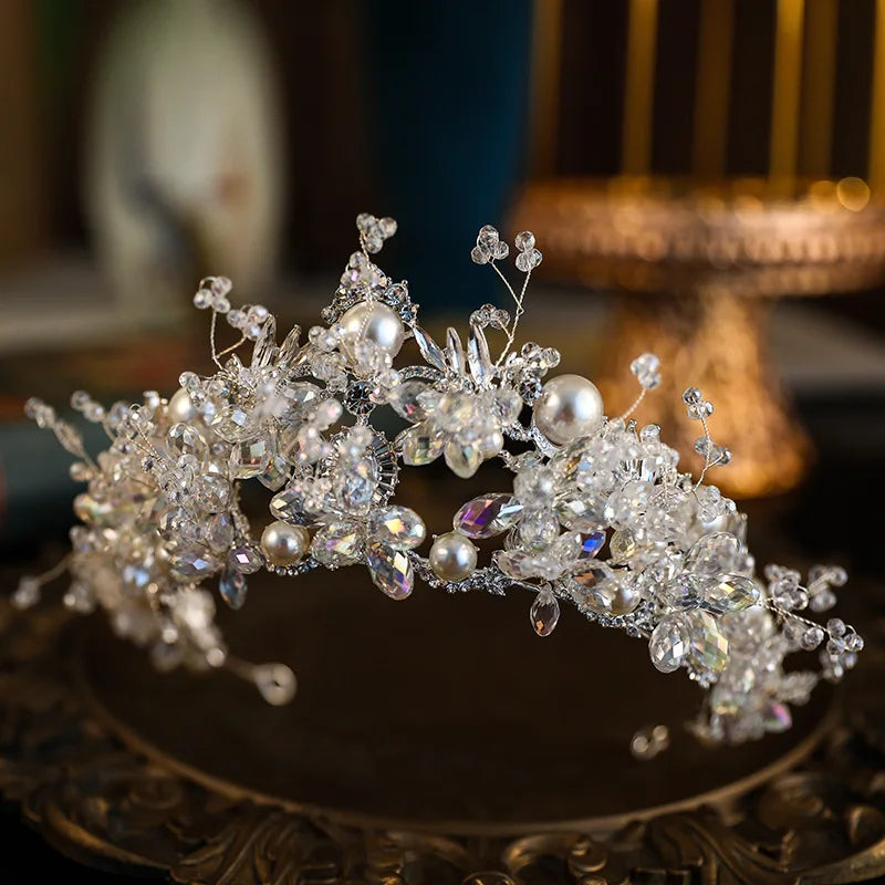 Three-quarter angle shot of an elegant princess crown wedding headband with reflective faceted crystals and polished cream pearls.