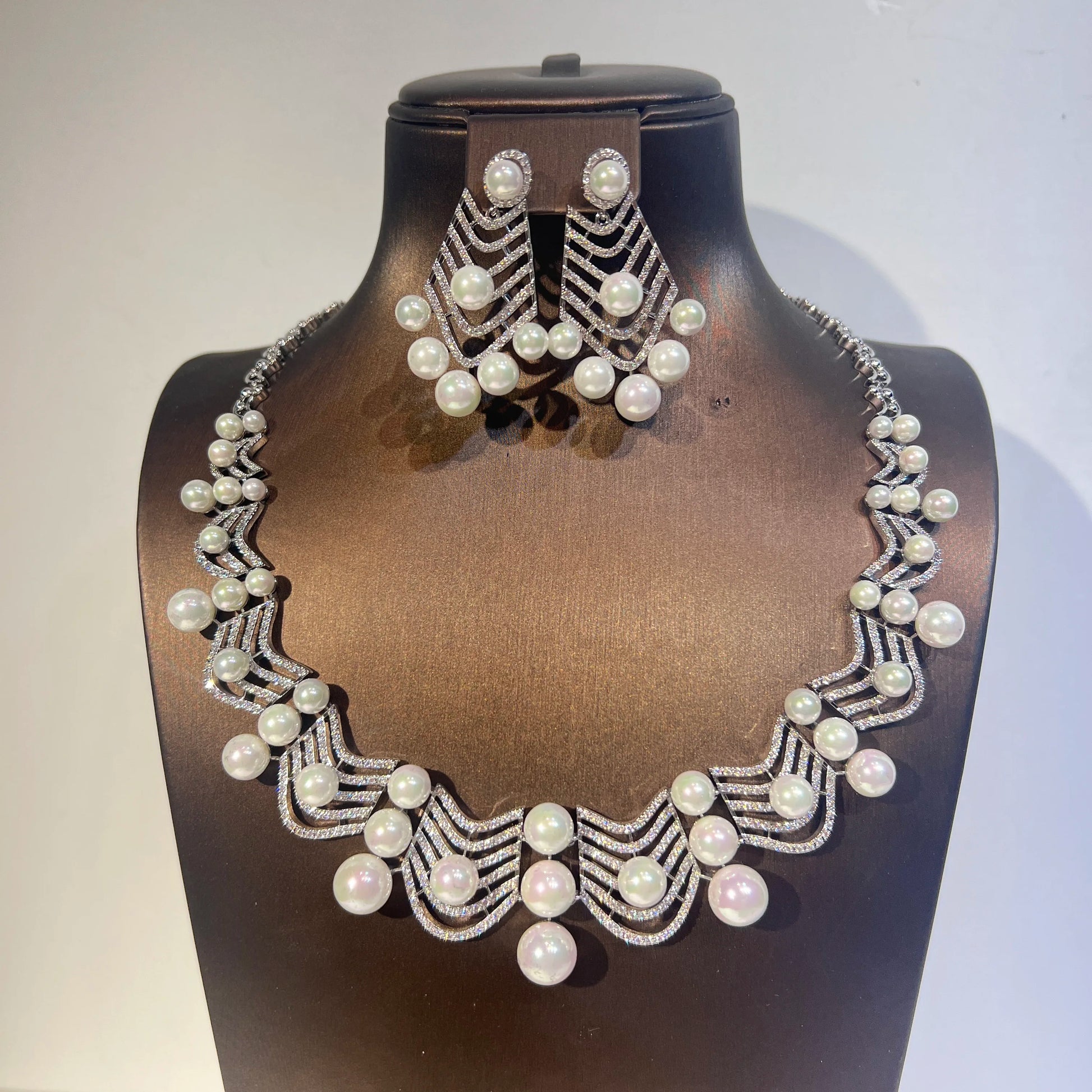 Side-angle display of a luxury silver cubic zirconia pearl wedding jewelry set for women against a light backdrop.