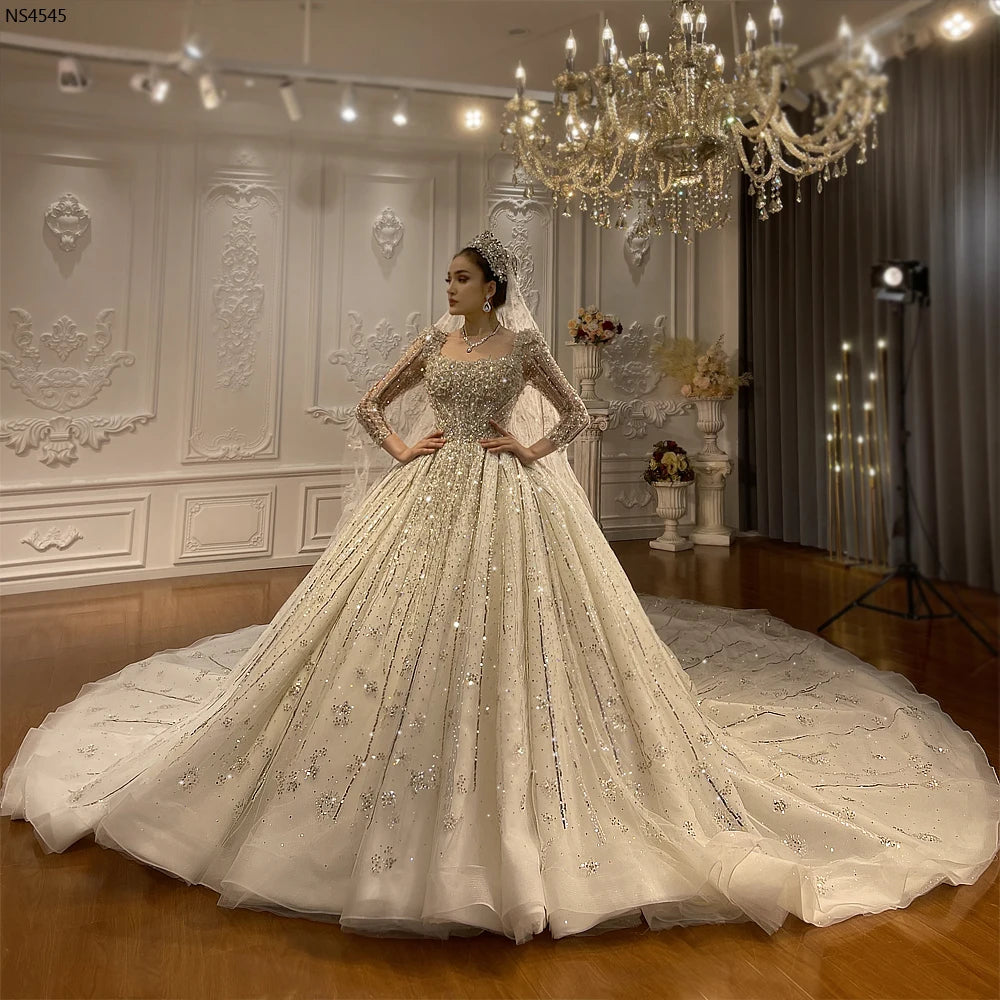 Full front view of a luxury Dubai ball gown wedding dress with a square neckline and long sleeves, featuring intricate silver crystal beading and a shimmering voluminous skirt.