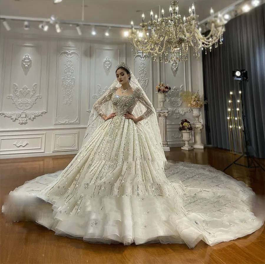 Close-up detail of a bridal gown bodice showcasing expert craftsmanship with dense hand-beaded crystals, a square collar, and shimmering illusion long sleeves.