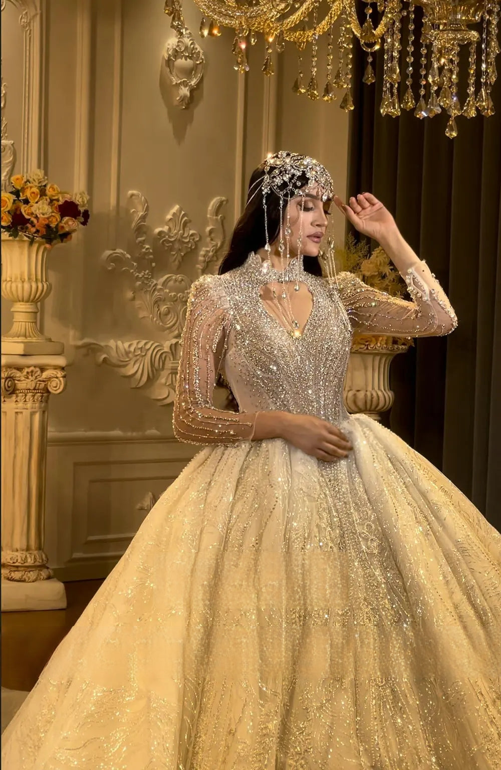Mid-length portrait of a bride posing in a long-sleeve luxury ball gown wedding dress, emphasizing the regal silhouette and the dense, intricate handwork beading across the bodice and sleeves.