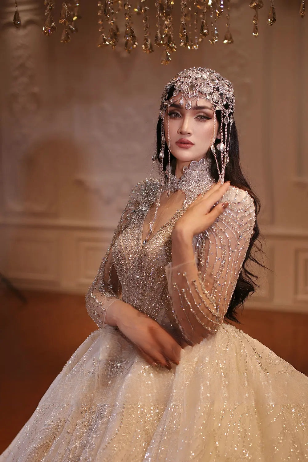 Close-up side profile of a bride wearing an exquisite heavy beaded wedding dress and matching crystal headpiece, highlighting the sheer beaded long sleeves and plunging V-neck illusion details.