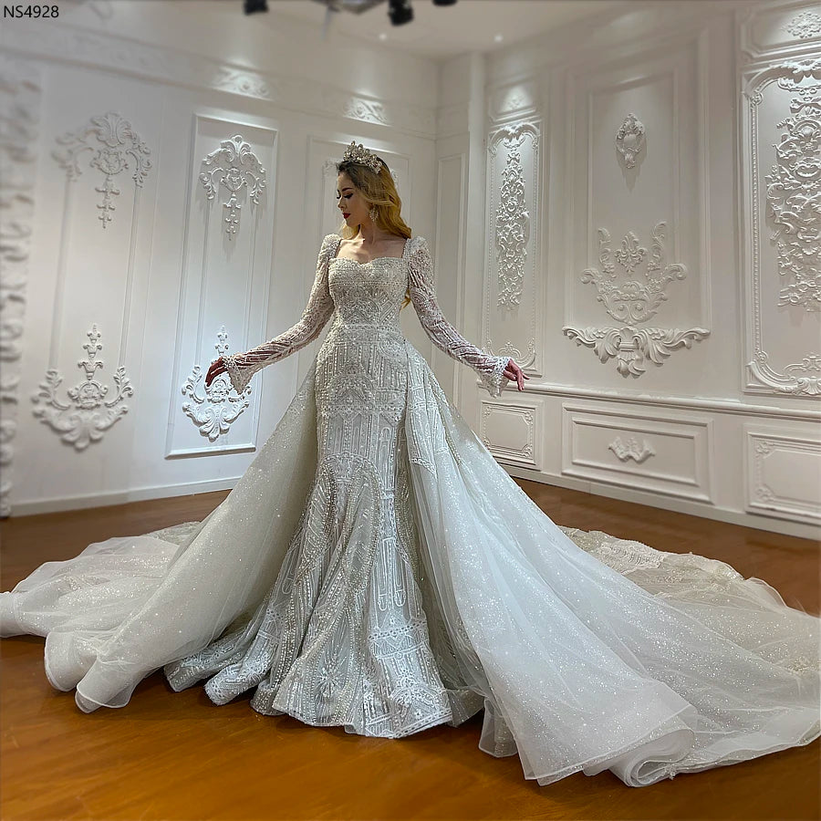 Wide-angle view of the luxury two-in-one convertible full lace wedding dress on a model, featuring a dramatic detachable ball gown overskirt and a long flowing train.