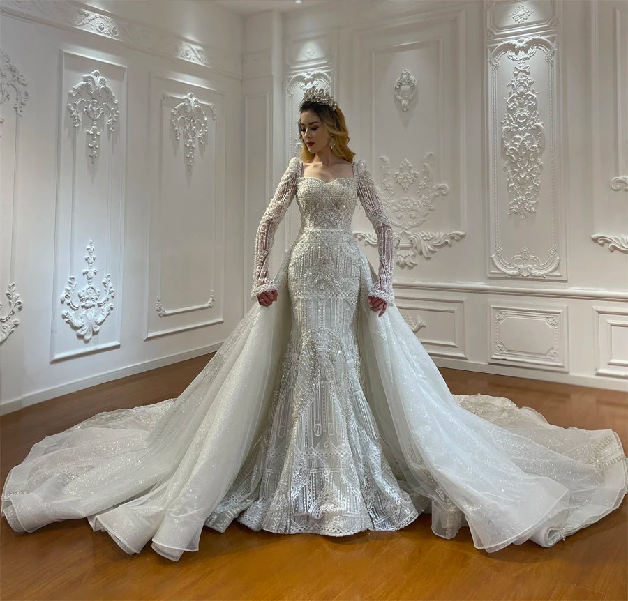 Front view close-up of a model wearing the luxury convertible full lace wedding dress with its voluminous detachable ball gown overskirt, displaying the grand, flowing silhouette.
