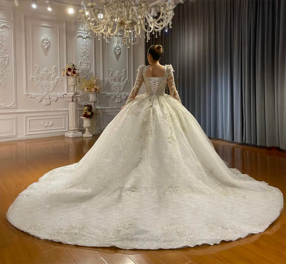Back view of the custom size bridal gown highlighting an elegant lace-up corset back, beaded long sleeves, and a massive, shimmering circular train.