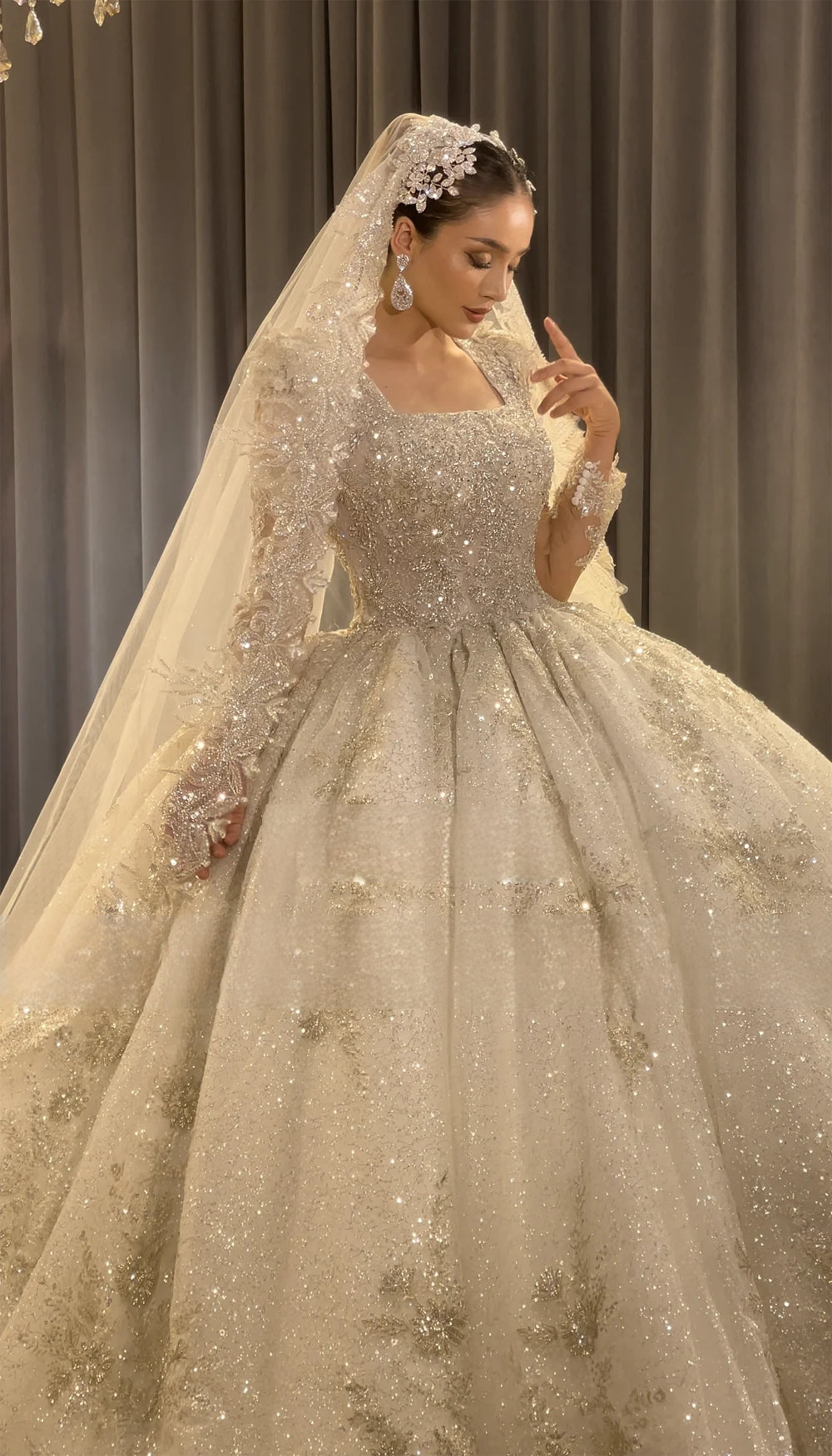 Close-up profile of a bride in the luxury handmade wedding dress, emphasizing the intricate crystal embroidery, sheer long sleeves, square neckline, and matching bridal veil.