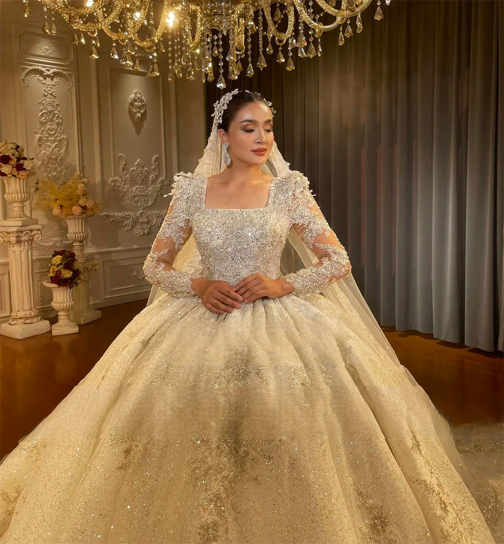 Front-facing medium shot of an elegant bride wearing a sparkling long-sleeve ball gown wedding dress with premium hand-beaded details and a flattering custom-fit bodice.