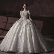 Full front view of a luxury international ball gown wedding dress featuring a square collar, long sleeves, and high-end shimmering fabric in a bridal showroom.