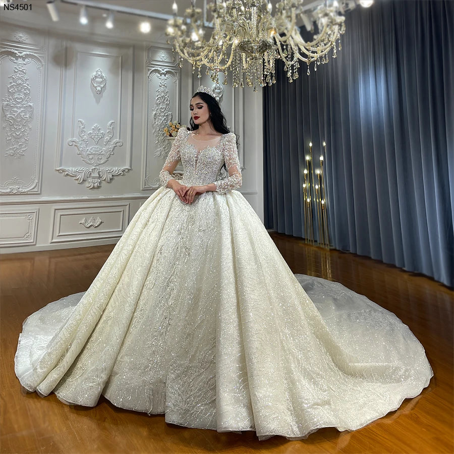 A glamorous bride wearing a luxury lace appliqued ball gown wedding dress with heavy crystal beading, long sleeves, and a sweeping cathedral train.