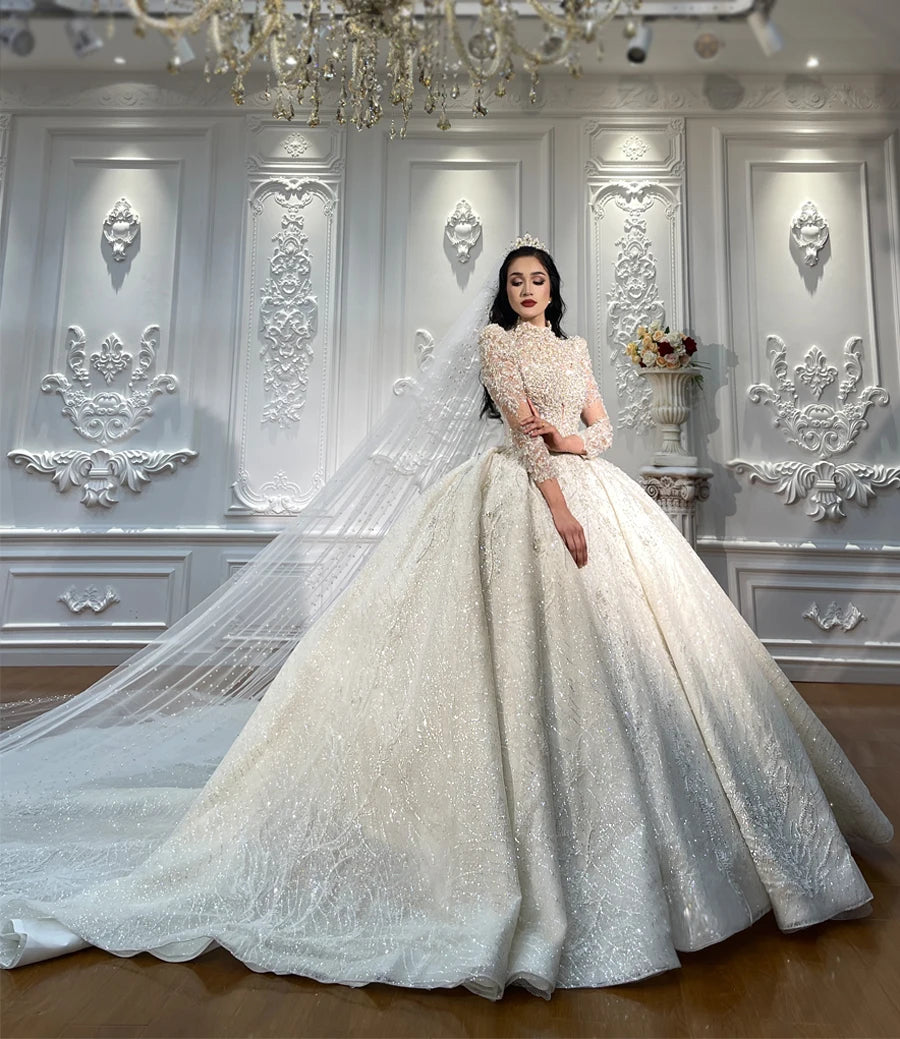 A bride elegantly poses in a luxury heavily beaded ball gown wedding dress featuring a long sparkling train and a traditional veil.
