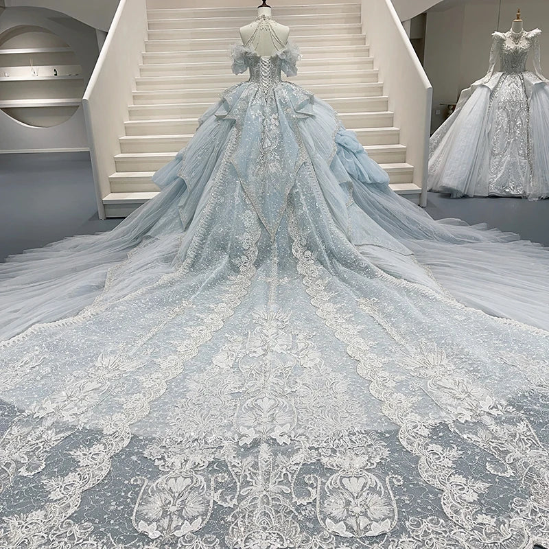 Full back view of a halter wedding dress on a mannequin, showcasing a dramatic open back, classic lace-up corset closure, and a grand cathedral train with lace borders.