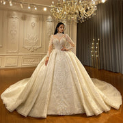 Front-side view of an elegant model wearing a luxury lace ball gown wedding dress with a high cover neck and sheer long sleeves, featuring intricate shimmering crystal embroidery and a voluminous skirt in a grand showroom.