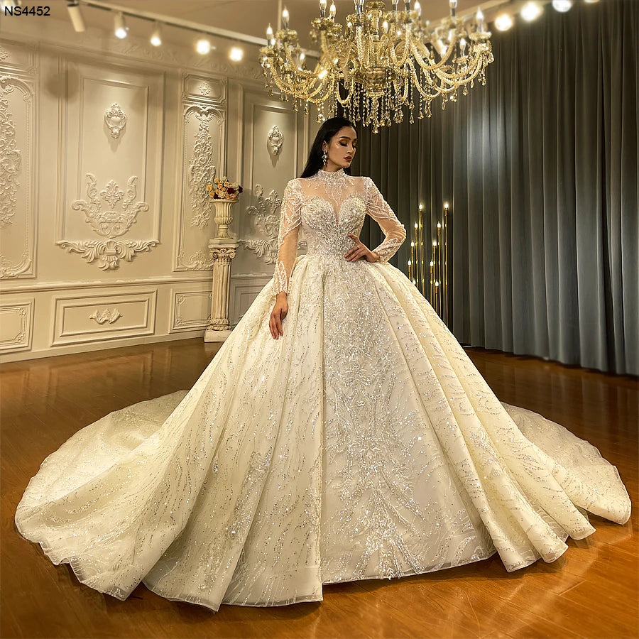 Full-length front view of a majestic long sleeve high neck bridal gown with a royal ball gown silhouette, showcasing dense sequin lace detailing and a massive cathedral-length train.