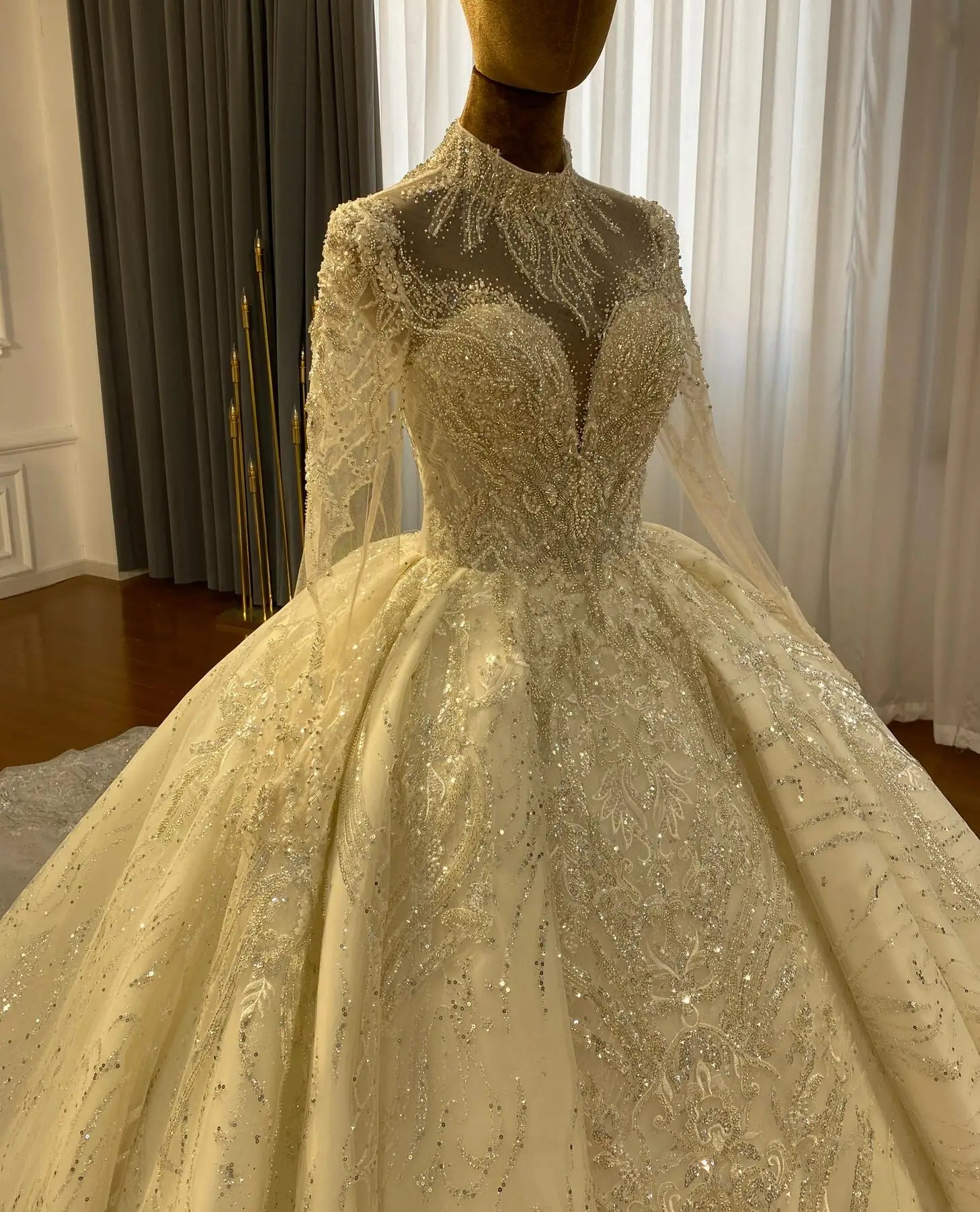 Close-up side perspective of a bridal gown bodice on a mannequin, showcasing the craftsmanship of the sheer lace long sleeves, high neck collar, and heavy hand-beaded crystal embellishments.