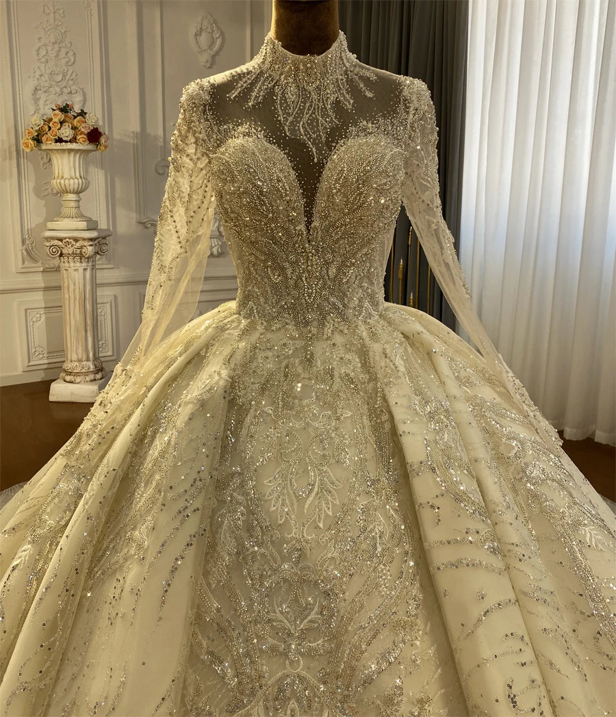 Detailed front view of a luxury wedding gown bodice, featuring an illusion sweetheart neckline under a high lace cover neck with shimmering silver thread and sequin embroidery.