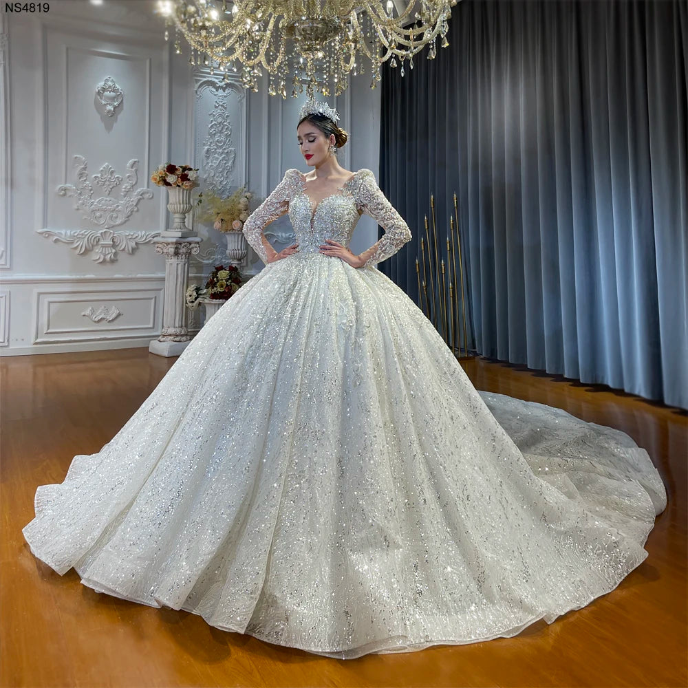 Front view of a luxury lace crystal ball gown wedding dress with long sleeves and a low cut neckline, featuring a voluminous shimmering skirt and intricate silver beading.