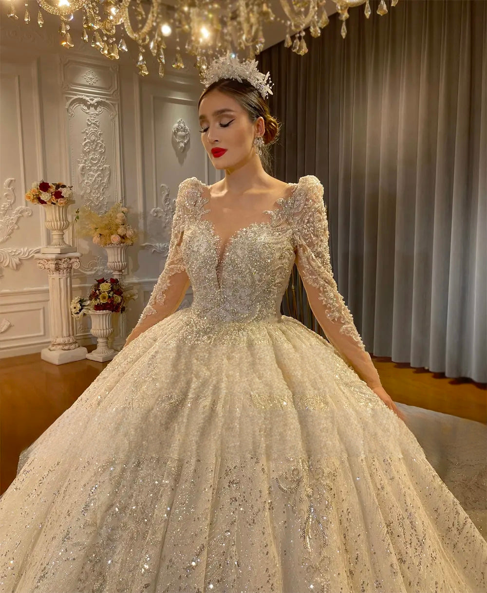 Elegant front close-up of a bride wearing a crystal ball gown wedding dress with a low cut neckline and long sleeves, adorned with a sparkling floral tiara.
