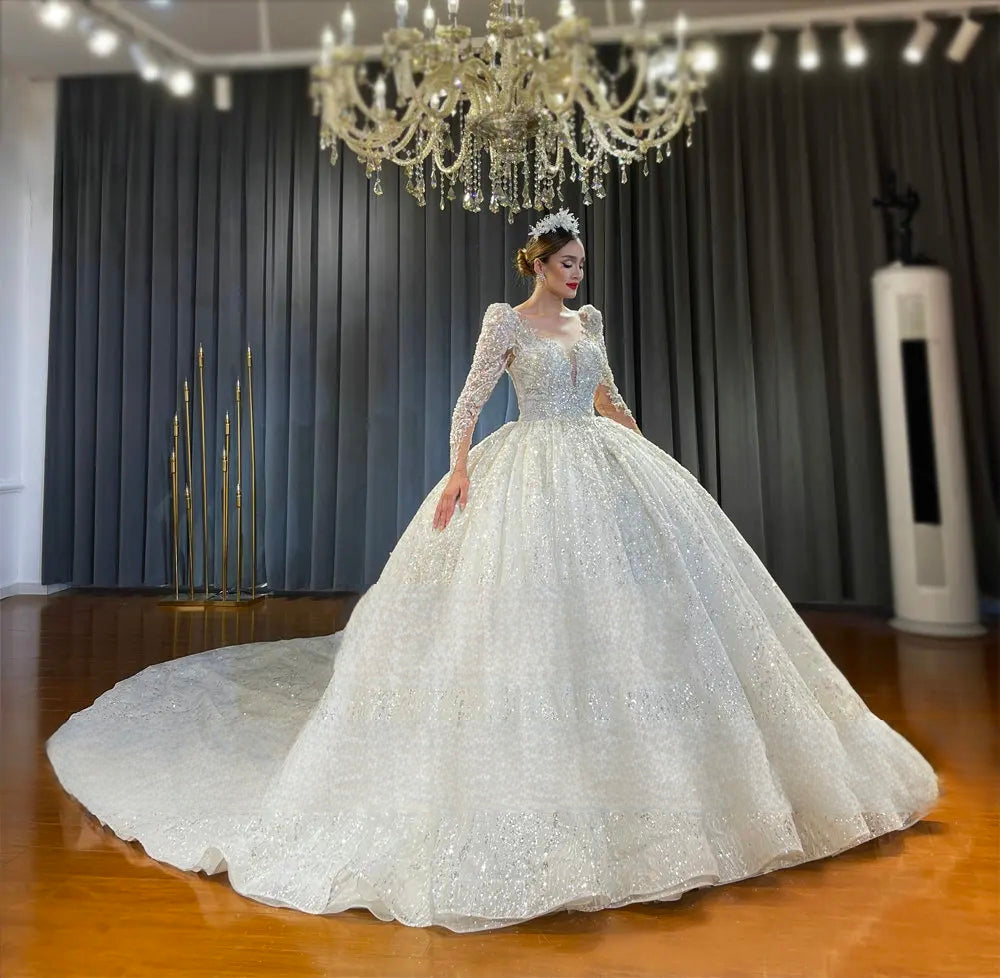 Wide side view of a princess-style luxury lace wedding dress with long sleeves, emphasizing the expansive circular long train spread across a wooden floor.
