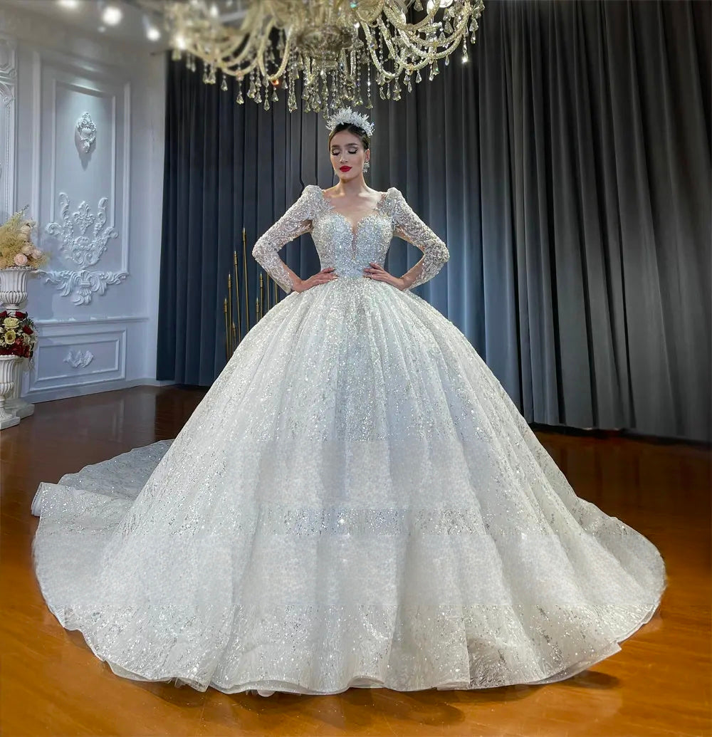 Majestic front perspective of a luxury crystal ball gown bridal dress with a voluminous sparkling skirt, long sleeves, and a plunging low cut neckline.