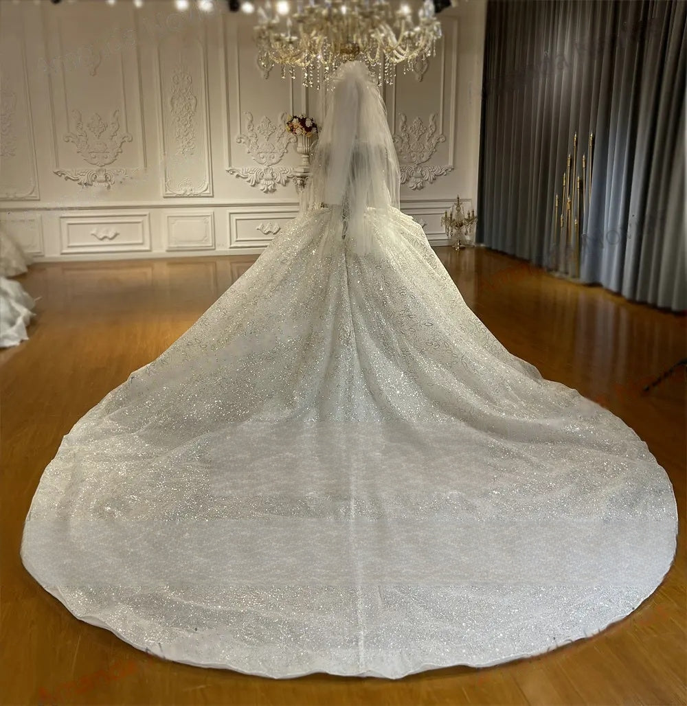 Side profile of an elegant bridal gown with an attached long lace cape, showcasing the voluminous shimmering skirt and intricate floral embroidery in a luxury studio
