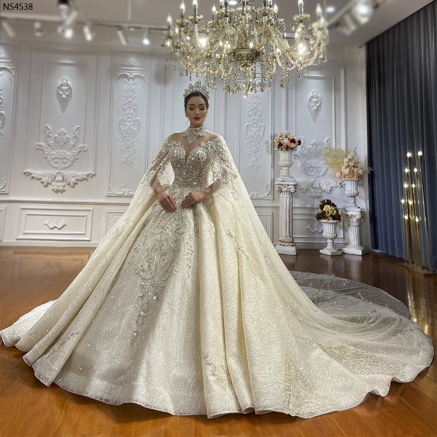 High-angle view of a luxury lace ball gown wedding dress with a high mandarin collar and a dramatic, floor-sweeping elegant long cape in a professional bridal studio.