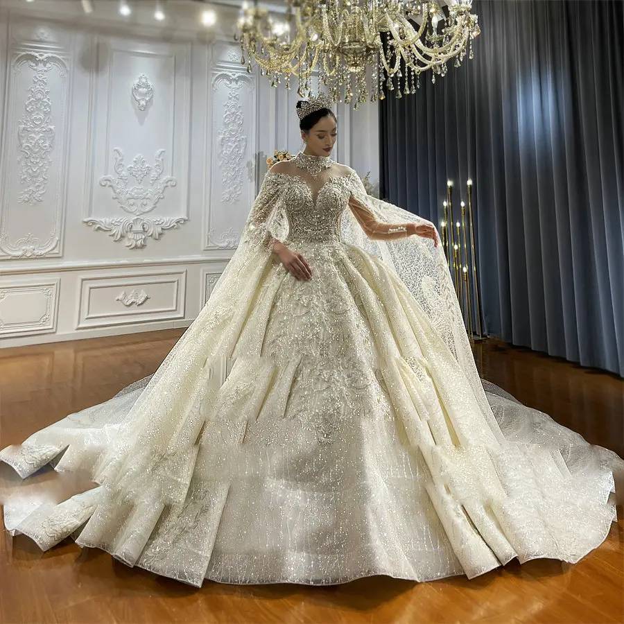 Angled side profile of a shimmering lace wedding dress highlighting the voluminous ball gown skirt and the matching floor-length bridal cape with intricate floral appliqués.
