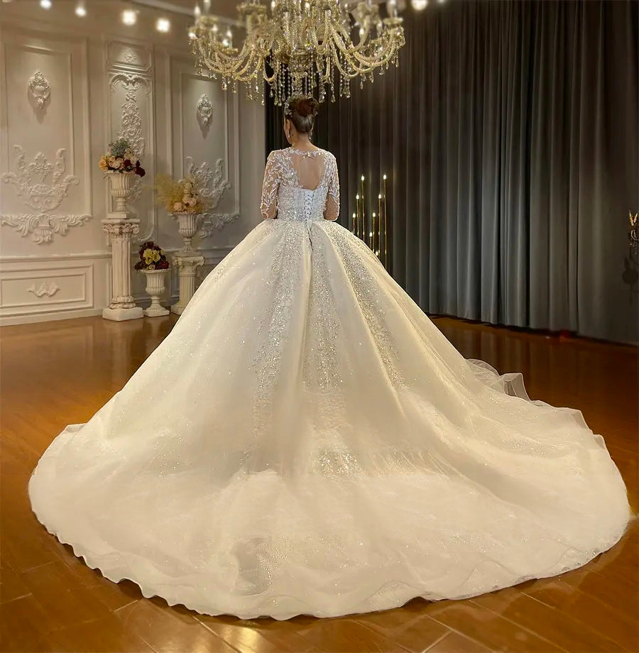 Full back perspective of a grand cathedral train on a sparkly ball gown bridal dress, featuring a classic corset back and intricate off-white lace detailing spread across the floor.