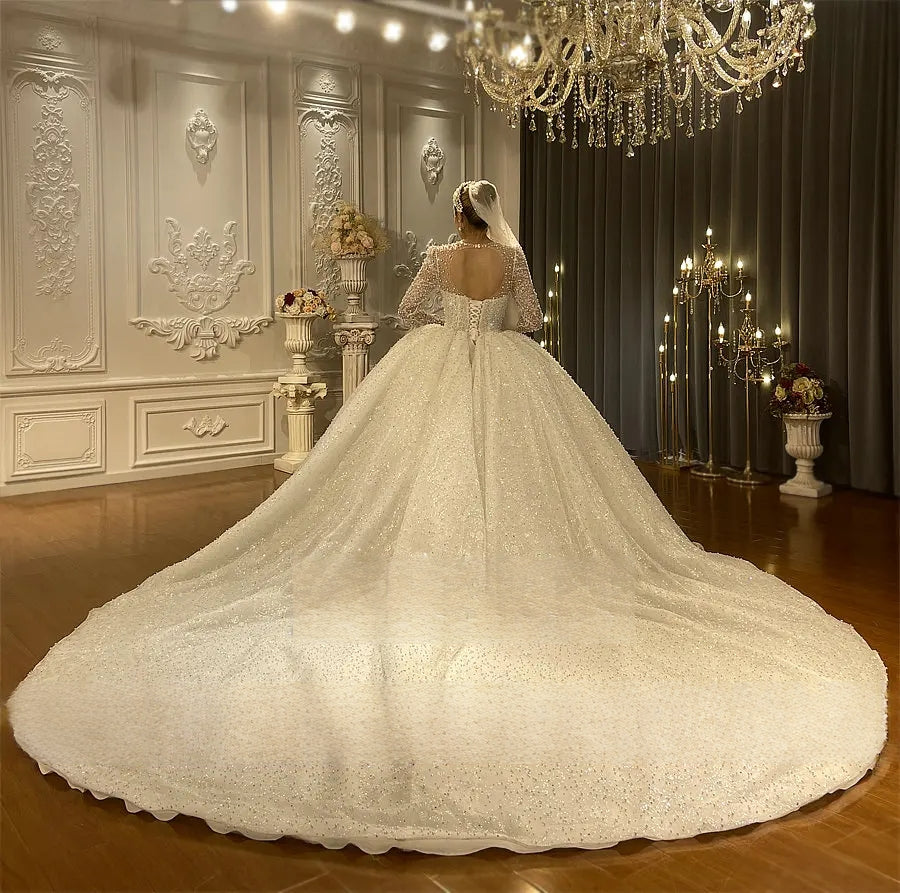 Back view of a regal pearl-embellished bridal gown highlighting an elegant corset back and a massive, shimmering cathedral-length train.
