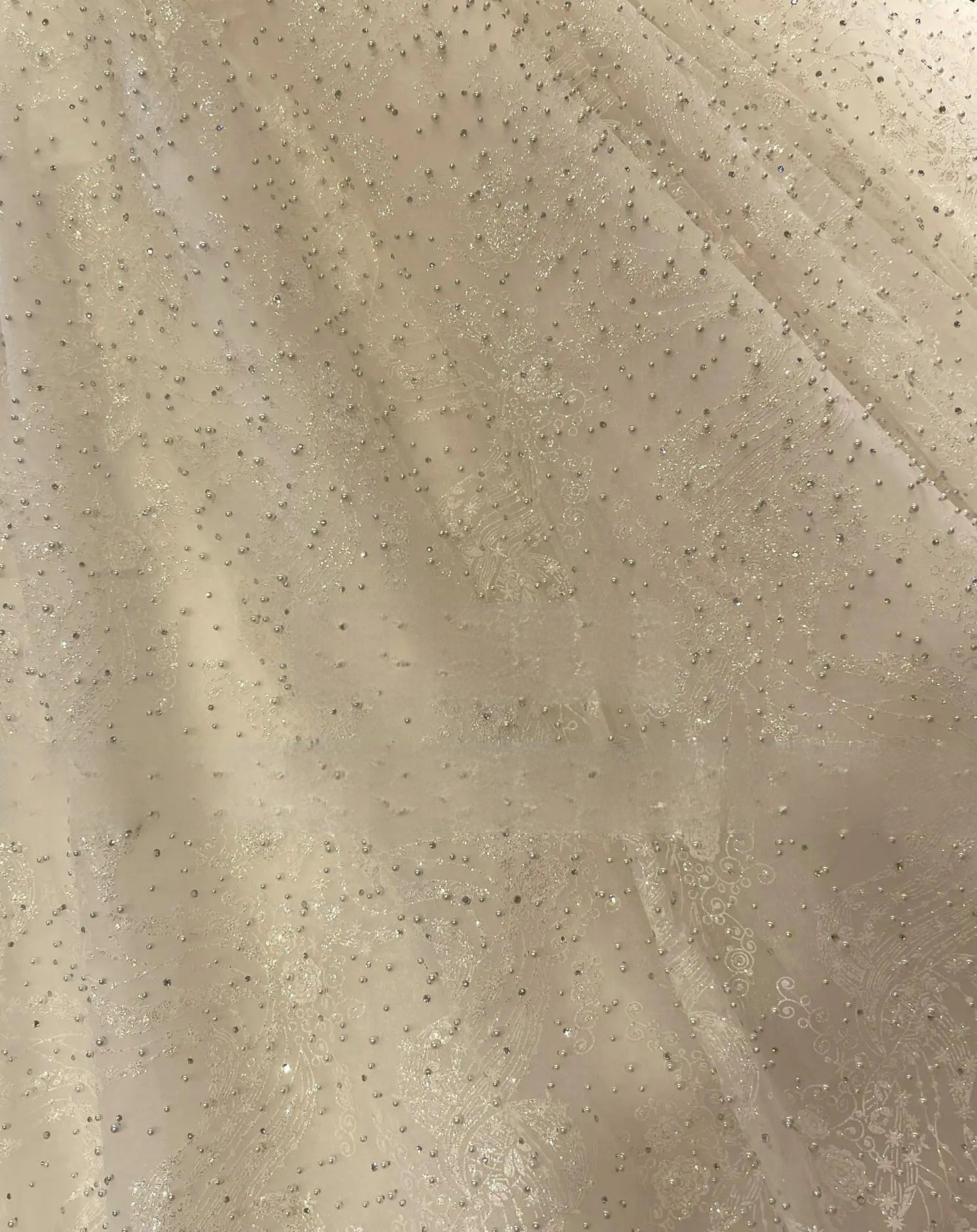 Macro close-up of luxury bridal fabric showcasing intricate lace patterns, sparkling sequins, and hand-sewn pearl beading.
