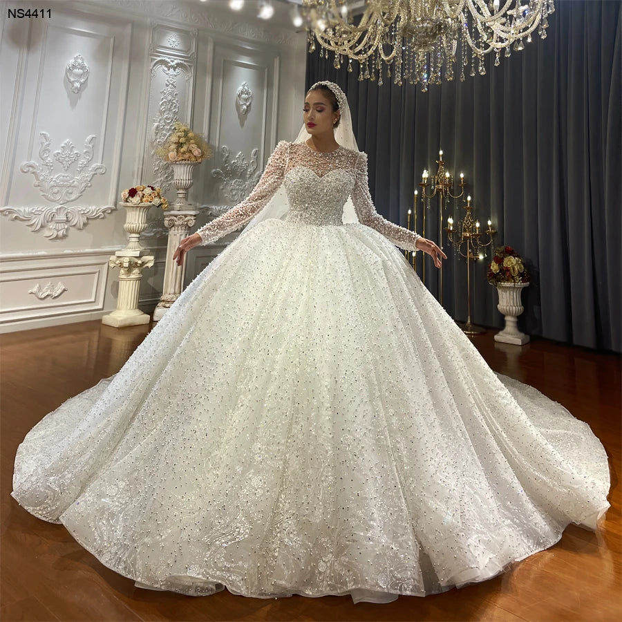 Full-length front view of a luxury long sleeve wedding dress with a voluminous ball gown silhouette and all-over pearl and crystal embellishments.