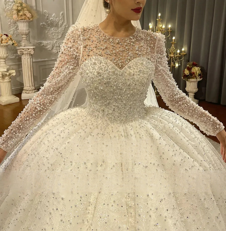 Close-up of the illusion bodice and long sleeves of a luxury wedding dress, featuring dense pearl beadwork and a sweetheart neckline design.