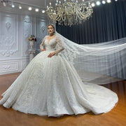 Full-length front view of a luxury long sleeve ball gown wedding dress featuring a voluminous sparkling skirt and an elegant lace-trimmed cathedral veil spread across a grand showroom.