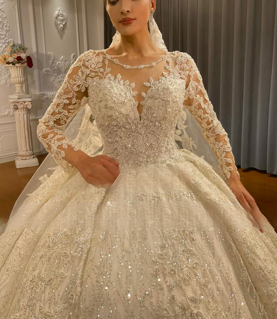 Close-up detail of the hand-beaded lace bodice and sheer illusion long sleeves on an elegant bridal gown, showcasing the intricate embroidery and shimmering crystal accents.