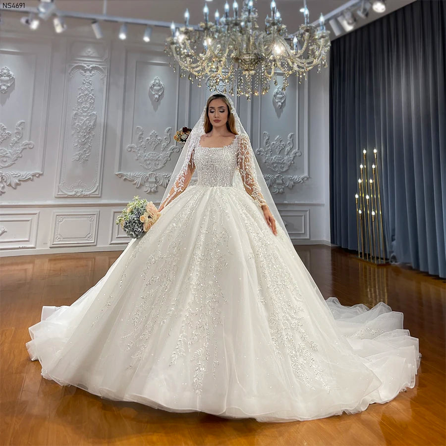Full-length front view of a luxury long sleeve ball gown wedding dress featuring exquisite lace appliques and elegant shimmering detailing in a grand bridal showroom.