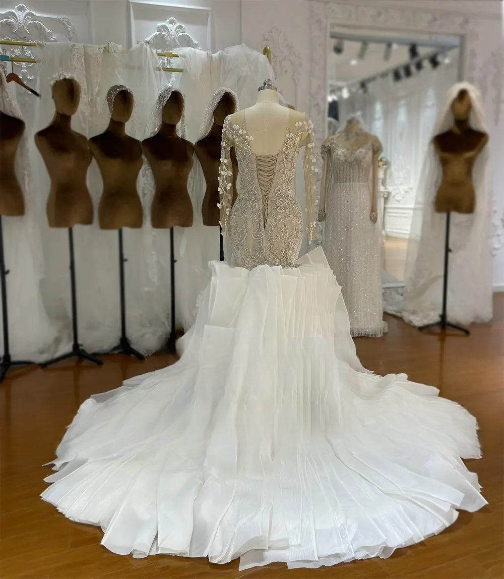 Rear perspective of a luxury mermaid bridal dress detailing the elegant corset closure and a massive cascading ruffled white train.