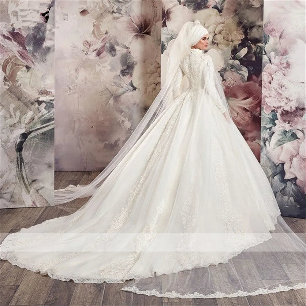 Rear view of a bride in a luxury Muslim A-line wedding dress featuring long sleeves, a high neck, and an extensive tulle train with lace applique beading.