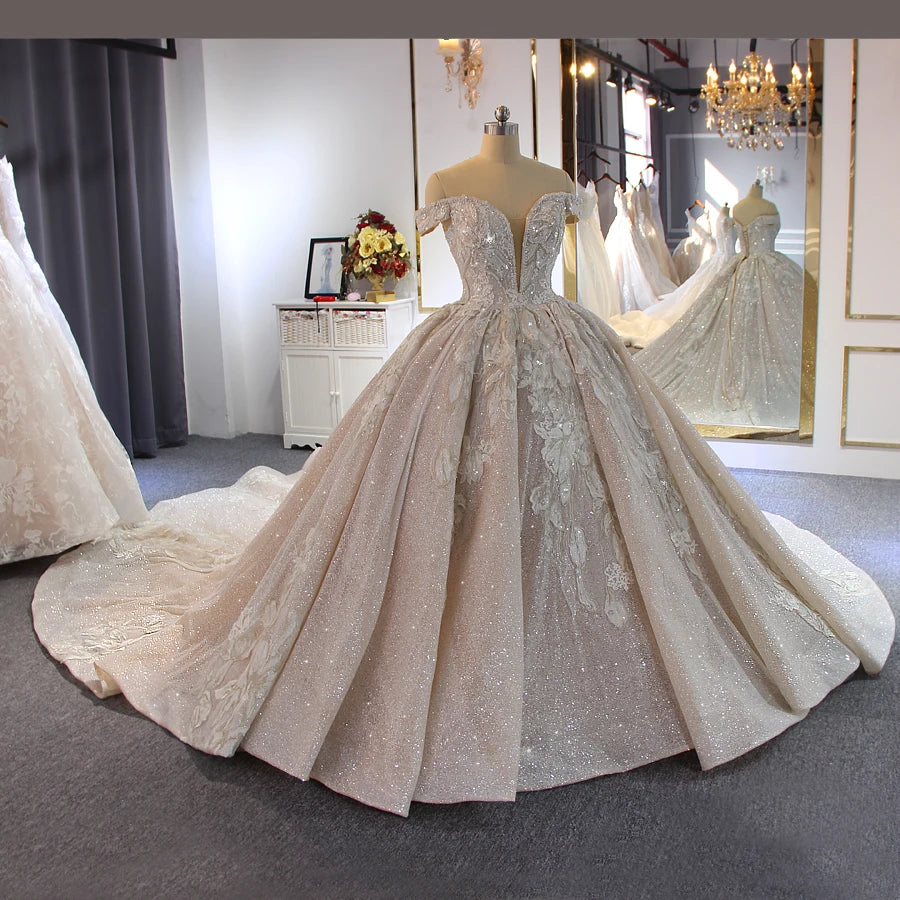 Front angled view of a champagne-colored luxury off-shoulder beaded wedding dress with an elegant long train displayed on a mannequin in a bridal showroom.
