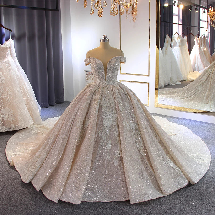 Full front view of a majestic off-the-shoulder ball gown wedding dress featuring heavy crystal beading, floral lace appliques, and a plunging V-neckline.