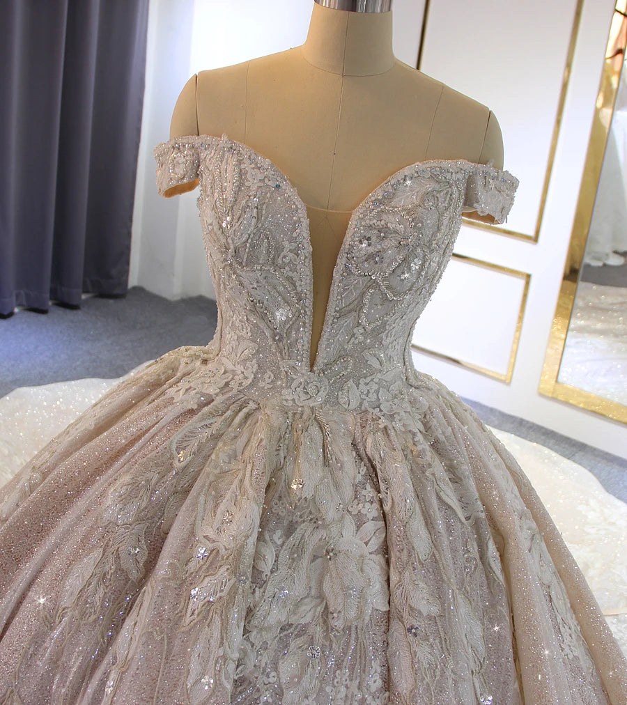 Close-up detail of the heavily beaded bodice on an off-shoulder luxury wedding dress, highlighting the shimmering crystals, floral lace, and deep illusion V-neck.