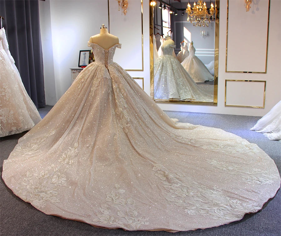 Dramatic wide-angle rear view of a luxury beaded ball gown wedding dress, showcasing the expansive, sparkling cathedral-length train on the showroom floor.