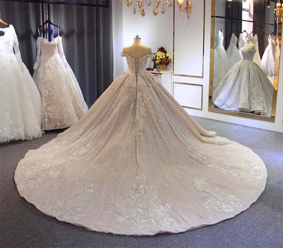 Full rear perspective of a champagne ball gown bridal dress on a mannequin, emphasizing the corset lace-up back and the grand, elegant long train.