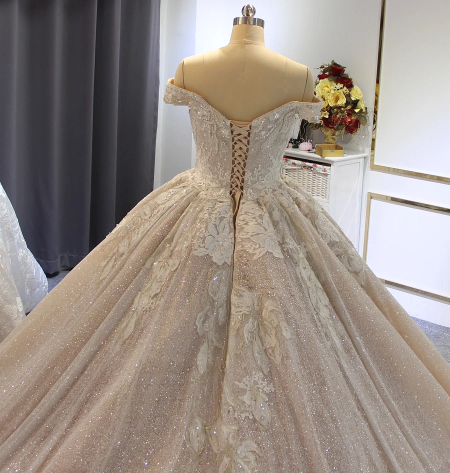 Close-up of the back of a luxury off-shoulder wedding dress, detailing the elegant lace-up corset closure surrounded by intricate floral lace and beadwork.