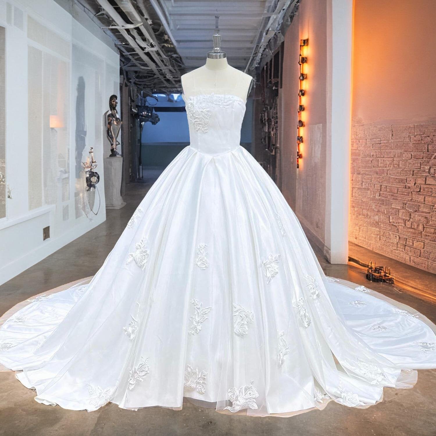 Full front view of a luxury off-shoulder boat neck ball gown wedding dress on a mannequin in a studio hallway, highlighting the classic satin silhouette and exquisite floral lace appliques.